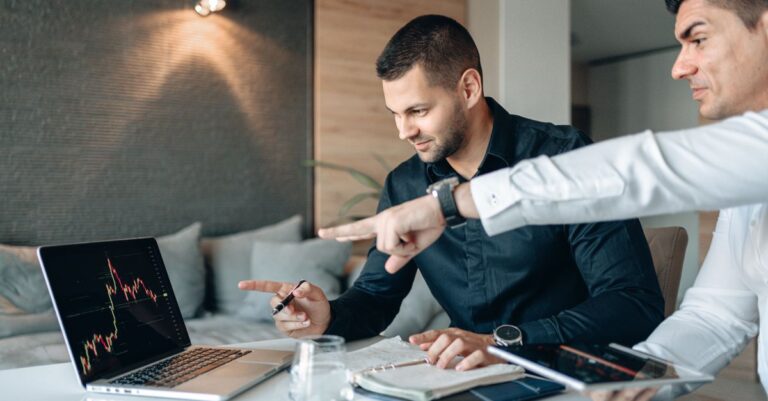 Dois homens discutindo dados financeiros em um laptop em um ambiente de trabalho moderno